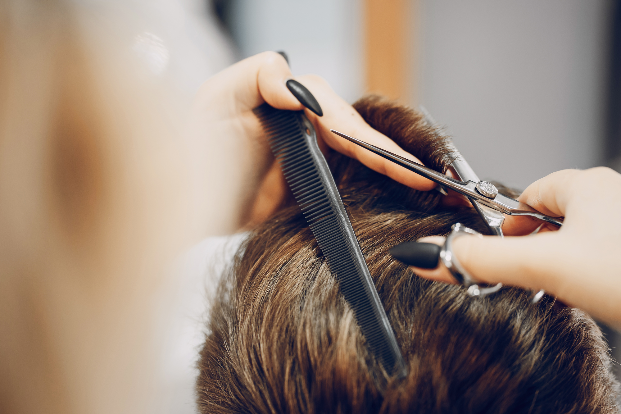 Friseur schneidet braunes Haar mit Schere und Kamm, fokussiert auf Hände, Werkzeuge und Haare im Salon.